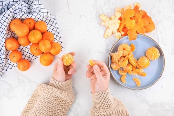 Mermer bir masada taze meyve ve mavi tabakla soyulmuş mandalina parçalarını tutan kadın ellerinin üst görüntüsü. Yüksek kalite fotoğraf