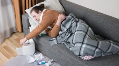 Kanepede yatıp burnunu mendile silen hasta bir adam. Haplar ve kullanılmış peçetelerle dolu pis bir zemin. Mevsimsel soğuk algınlığı, virüs ve evde tedavi kavramı. Yüksek kalite 4k görüntü