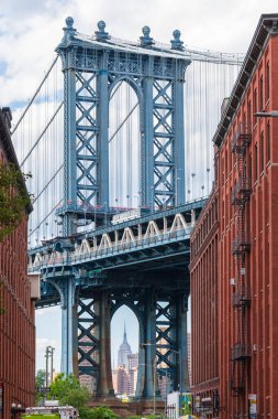 Uzak Empire State binasını çerçeveleyen Manhattan Köprüsü 'nün yüksek kontrastlı görüntüsü ön planda DUMBO, Brooklyn' deki yeşil park alanlarını gösteriyor..