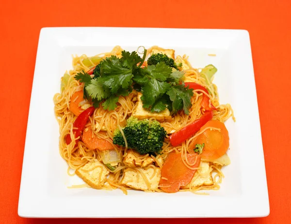 Kızarmış tofu, brokoli, havuç ve biberle karıştırılmış ve beyaz tabakta taze kişniş ile süslenmiş vermicelli pirinç eriştesi stüdyo manzarası. Sağlıklı, vejetaryen Asya mutfağına uygundur..