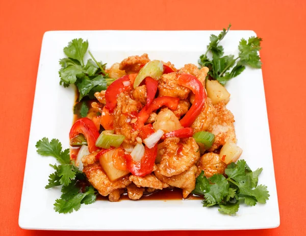 Taze biber, soğan ve ananasla karıştırılmış bol yağda kızartılmış ve ekşi tavuk parçaları beyaz bir tabakta kişniş garnitürle servis ediliyor. Çin mutfağı ve lezzetli yemek kavramları için mükemmel..