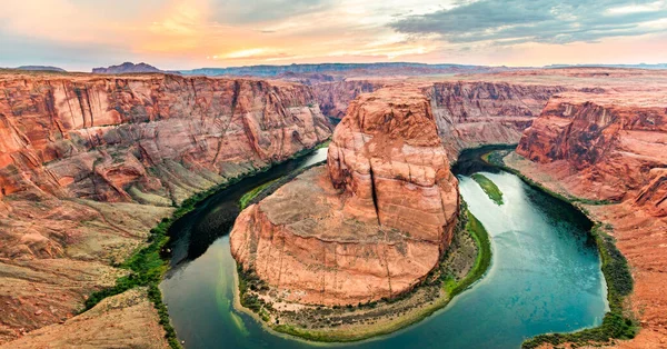 Horseshoe Bend 'in geniş açılı geniş açılı HDR görüntüsü batan güneşin güçlü, sıcak parıltısıyla aydınlatılan canlı kırmızı uçurumları vurguluyor..