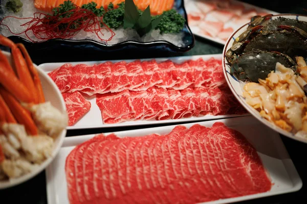 İnce dilimlenmiş kırmızı sığır eti, buzlu somon balığı, yengeç ve istiridye gibi çeşitli taze, ham malzemeler, açık büfe ya da sıcak tencere teması için ideal tabakta dizilmiş..