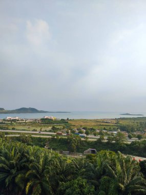 Yeşil tepeler, tropik bitki örtüsü ve bulutlu bir gökyüzünün altında sakin bir deniz manzarası.