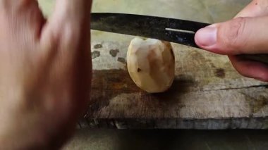 Yakından çekilmiş bir fotoğraf, beton bir yüzey üzerinde bıçakla cassava (yucca kökü) soyan birini gösteriyor..