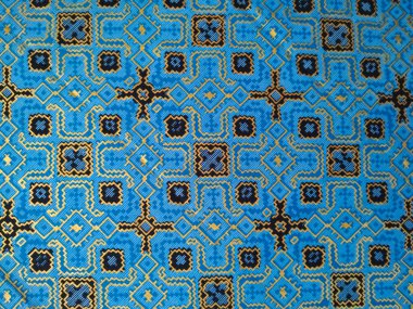 Altın ve siyahta karmaşık geometrik desenlere sahip mavi dokuma kumaş, simetrik motiflerle geleneksel etnik tekstil sanatını sergiliyor..