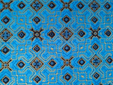 Altın ve siyahta karmaşık geometrik desenlere sahip mavi dokuma kumaş, simetrik motiflerle geleneksel etnik tekstil sanatını sergiliyor..