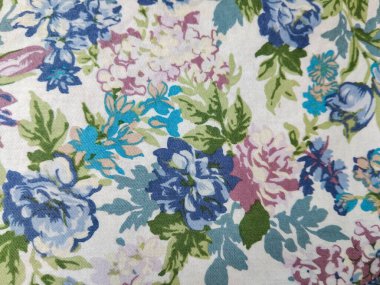 Beyaz arka planda yeşil yapraklı mavi, mor ve pembe çiçeklerden oluşan renkli bir kumaş deseni.