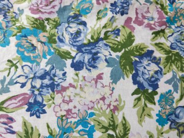 Beyaz arka planda yeşil yapraklı mavi, mor ve pembe çiçeklerden oluşan renkli bir kumaş deseni.