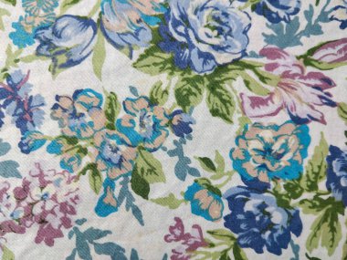 Beyaz arka planda yeşil yapraklı mavi, mor ve pembe çiçeklerden oluşan renkli bir kumaş deseni.