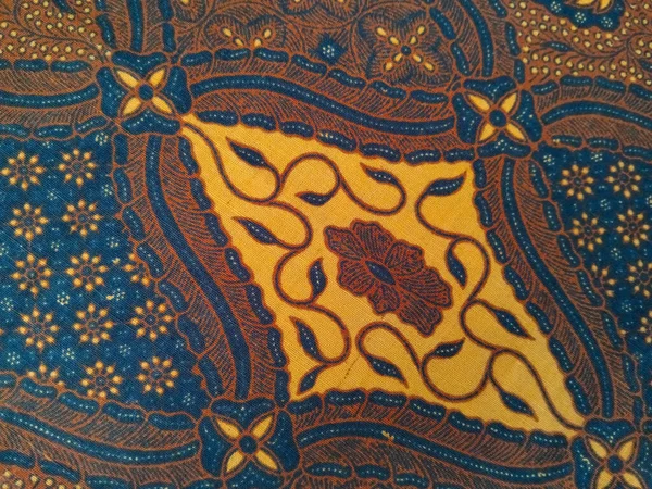 Karmaşık kahverengi, mavi ve sarı desenli geleneksel batik kumaş, simetrik dizaynlı çiçekli ve geometrik motifler.