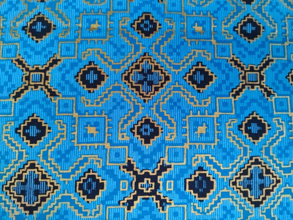 Altın ve siyahta karmaşık geometrik desenlere sahip mavi dokuma kumaş, simetrik motiflerle geleneksel etnik tekstil sanatını sergiliyor..
