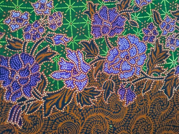Mor çiçek desenli renkli batik kumaş, kahverengi yapraklar, ve karmaşık yeşil geometrik arka plan, geleneksel Endonezya tekstil sanatını sergiliyor..
