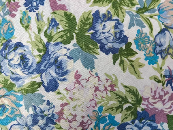 Beyaz arka planda yeşil yapraklı mavi, mor ve pembe çiçeklerden oluşan renkli bir kumaş deseni.