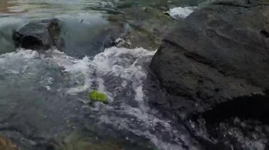 Nehir suyunun akışını yakından görmek dinamik dalgalanmalar yaratır ve karanlık kayaların üzerinde hareket ederken su sıçratır.