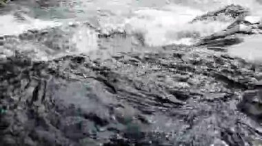 Nehir suyunun akışını yakından görmek dinamik dalgalanmalar yaratır ve karanlık kayaların üzerinde hareket ederken su sıçratır.