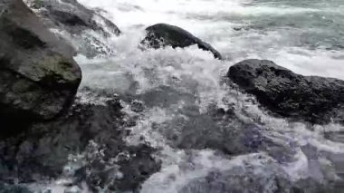 Nehir suyunun akışını yakından görmek dinamik dalgalanmalar yaratır ve karanlık kayaların üzerinde hareket ederken su sıçratır.