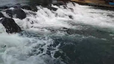 Nehir suyunun akışını yakından görmek dinamik dalgalanmalar yaratır ve karanlık kayaların üzerinde hareket ederken su sıçratır.