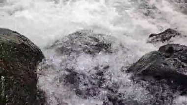 Nehir suyunun akışını yakından görmek dinamik dalgalanmalar yaratır ve karanlık kayaların üzerinde hareket ederken su sıçratır.