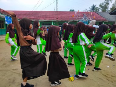 LAMPUNG, INDONESIA - 03 Ağustos 2025: Bir okul etkinliği sırasında bir grup yeşil üniformalı ve kahverengi tesettürlü öğrenci ayakta duruyor. Endonezya 3 Ağustos 2025.