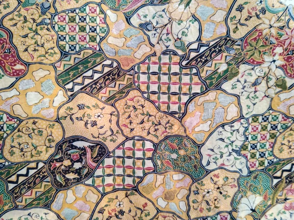 Karmaşık çiçek ve yaprak motifleri ile renkli batik kumaş, yeşil, mavi, kırmızı ve sarı desenli uyumlu geleneksel tasarım.