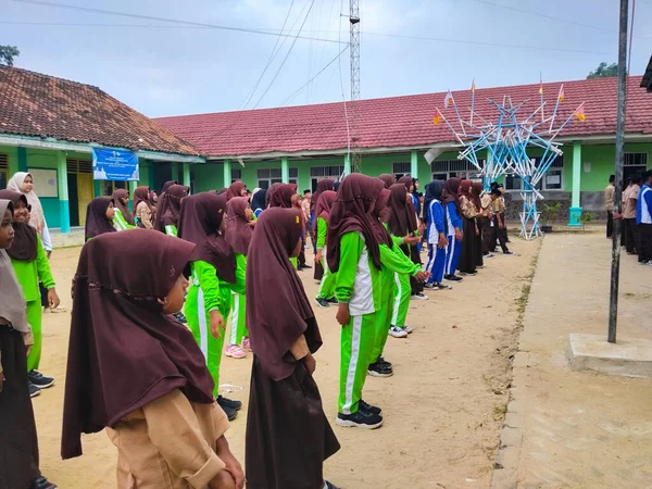 LAMPUNG, INDONESIA - 03 Ağustos 2025: Bir okul etkinliği sırasında bir grup yeşil üniformalı ve kahverengi tesettürlü öğrenci ayakta duruyor. Endonezya 3 Ağustos 2025.