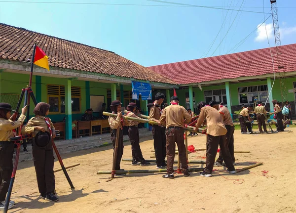 Bir grup Endonezyalı izci, kırmızı iplerle bağlanmış mavi ve beyaz direklerle bir yapı inşa etmek için açık havada birlikte çalışıyorlar.