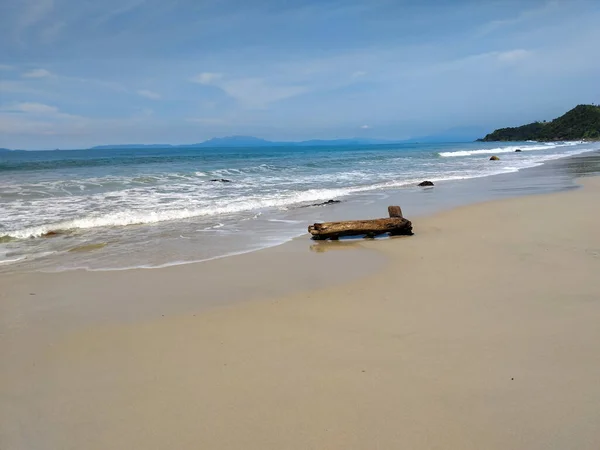 Yumuşak okyanus dalgalarının berrak mavi gökyüzünün altında kumlu bir sahile vuruşunun huzurlu görüntüsü.