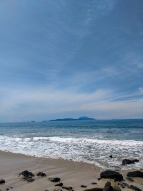 Berrak mavi gökyüzü ve turkuaz deniz suyuyla kayalık tropikal bir sahilin manzarası..