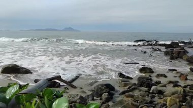 Sakin okyanus dalgaları parlak bir gökyüzünün altında kumlu bir sahile vuruyor.