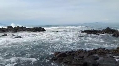 Berrak mavi gökyüzü ve turkuaz deniz suyuyla kayalık tropikal bir sahilin manzarası..