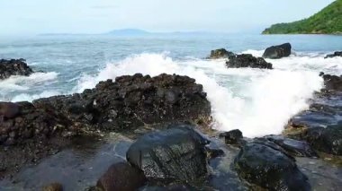 Berrak mavi gökyüzü ve turkuaz deniz suyuyla kayalık tropikal bir sahilin manzarası..