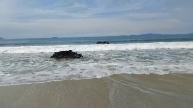 Okyanus dalgalarının sakin manzarası açık mavi bir gökyüzünün altındaki kumlu bir sahile nazikçe çarpıyor.