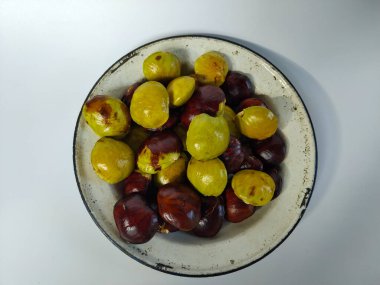 Çeşitli yeşil ve kahverengi tonlarında taze jengkol (köpek meyvesi) ile dolu rustik bir diş minesi plakasının üst görüntüsü