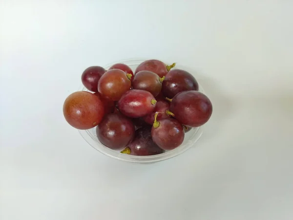 Temiz beyaz arka plana yerleştirilmiş taze kırmızı üzümlerle dolu şeffaf bir plastik kasenin yakın plan çekimi.