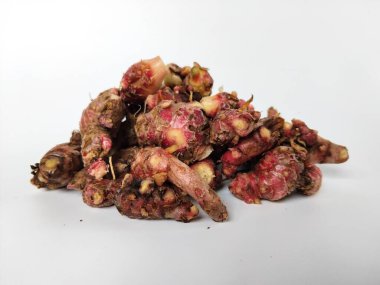 Temiz beyaz arka plana yerleştirilmiş taze toplanmış kırmızı galangal köklerinin yakın plan görüntüsü.