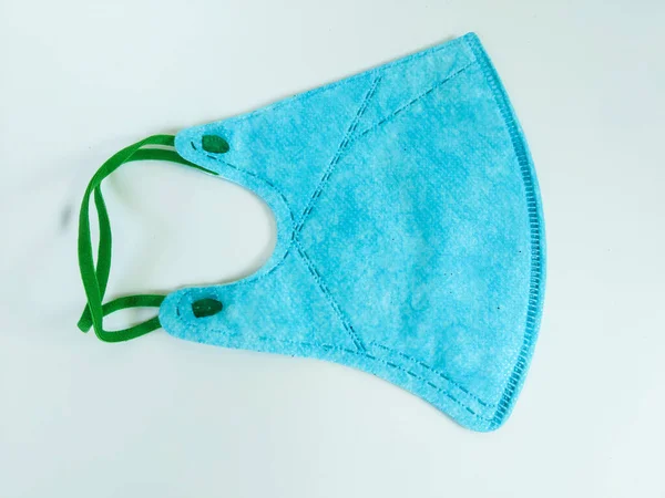 Yeşil elastik kulak düğümlü mavi koruyucu bir yüz maskesi temiz beyaz bir arkaplanda sergilenir
