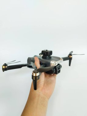 Temiz beyaz bir arkaplana karşı bir el tarafından tutulan kompakt kuadkopter insansız hava aracının yakın çekim görüntüsü.