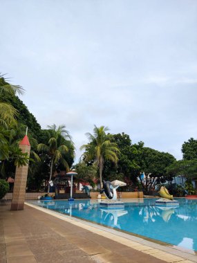 Bereketli tropik palmiye ağaçları ve yeşilliklerle çevrili sakin bir açık yüzme havuzu.