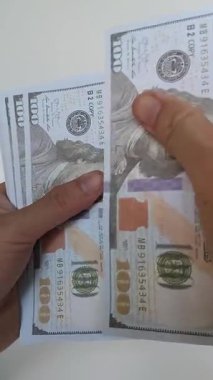 Beyaz arka planda birkaç yüz dolarlık banknotları sayarken iki elin yakın çekimi.