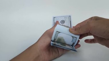 Temiz beyaz arka planda 100 dolarlık banknotları çeviren bir elin yakın çekimi.