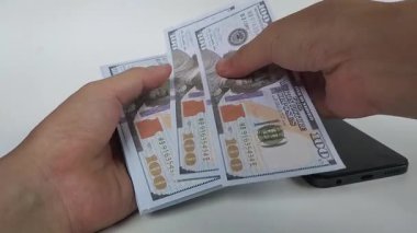 Beyaz arka planda birkaç yüz dolarlık banknotları sayarken iki elin yakın çekimi.