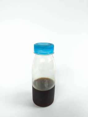 Açık plastik bir şişe, mavi bir vida kapağı, kısmen koyu kahverengi bir sıvıyla doldurulmuş, temiz beyaz arka planda fotoğraflanmış.