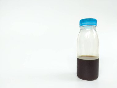 Açık plastik bir şişe, mavi bir vida kapağı, kısmen koyu kahverengi bir sıvıyla doldurulmuş, temiz beyaz arka planda fotoğraflanmış.