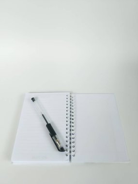 Boş bir spiral defterin minimalist düz uzantısı ve temiz beyaz bir yüzeye yerleştirilmiş siyah bir kalem.