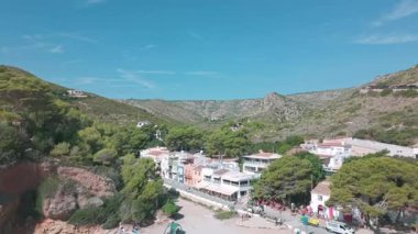 Güneşli bir yaz gününde İspanya 'nın Javea plajı yakınlarındaki Cala Granadella köyünün ve çevreleyen yeşil tepelerin insansız hava aracı görüntüleri. Javea, İspanya - 4 Ekim 2025.