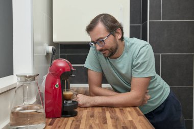 Modern mutfakta kahve makinesiyle kahve yapan adam. Evde espresso hazırlayan ve bir fincan taze kahvenin tadını çıkaran biri. Sabah rutini, ev konforu ve kafein enerjisi kavramı