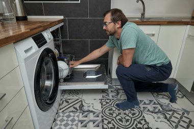 Modern mutfakta bulaşık makinesini yükleyen adam. Ev işleri yapan, bulaşık yıkayan ve evde mutfak gereçleri düzenleyen biri. Ev hayatı kavramı, ev temizliği ve modern yaşam tarzı..