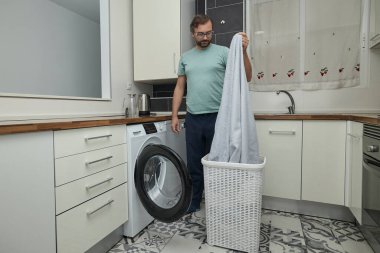 Modern mutfakta çamaşır yıkayan bir adam. Çamaşır makinesini yükleyen ve deterjan dolduran kişi. Ev işleri, ev hayatı ve ev temizliği kavramı