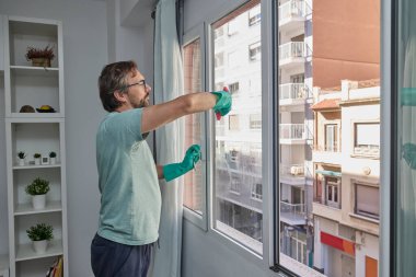 Evdeki pencereleri temizleyen adam. Lastik eldiven giyen, bardağı sünger ve spreyle yıkayan biri. Birlikte ev işi yapan bir çift. Ev temizliği, hijyen ve ev hayatı kavramı
